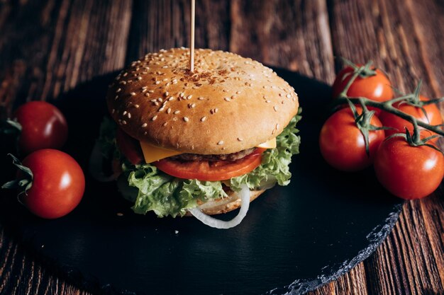 Hamburger z sałatą, pomidorem i cebulą na czarnym talerzu.