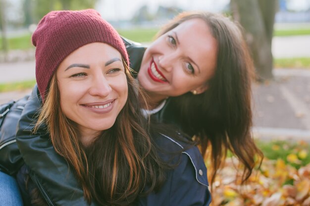 Happy Beautiful Girls siedzi jesienią w żółtych liściach na trawniku w mieście.