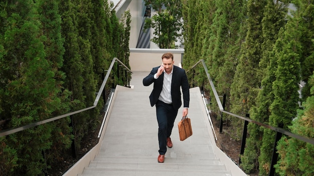 Zdjęcie happy businessman walking up stair and calling manager by using phone urbane