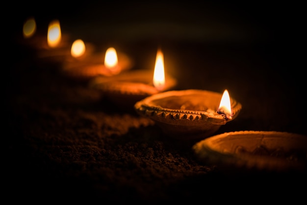Happy Diwali - wiele lamp z terakoty lub lamp naftowych ułożonych na glinianej powierzchni lub ziemi w jednej linii lub zakrzywionej lub zygzakowatej formie, selektywne skupienie