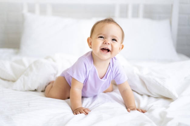 Happy little cute girl dziecko w Body siedzi na łóżku na białej pościeli, uśmiechając się. Pojęcie produktów dla dzieci.