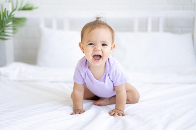 Happy little cute girl dziecko w Body siedzi na łóżku na białej pościeli, uśmiechając się. Pojęcie produktów dla dzieci.