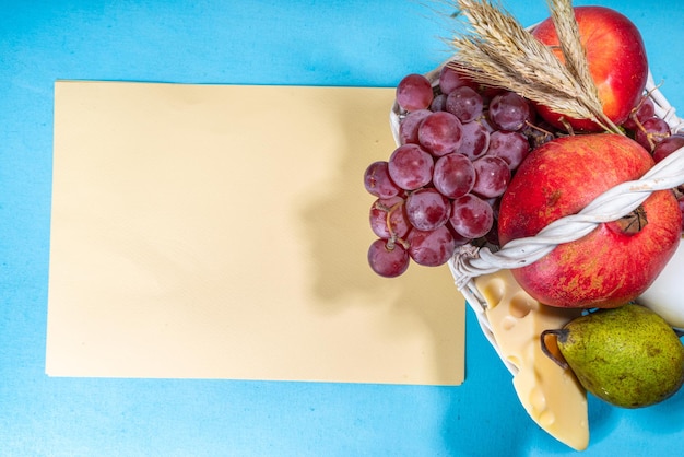 Zdjęcie happy shavuot kartkę z życzeniami z jedzeniem symbole żydowskiego szawuot wakacje granat winogrona jabłko słodka chałka chleb pszenica kłosy mleko ser twaróg na jasnoniebieskim tle
