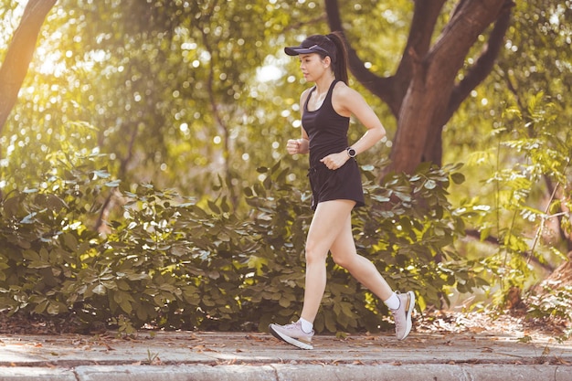 Happy uśmiechnięta dorosła kobieta Azji jogging na świeżym powietrzu w parku miejskim w piękny letni dzień w promieniach słońca. Szczęśliwa zrelaksowana dojrzała kobieta biegająca, aby prowadzić aktywny i zdrowy tryb życia