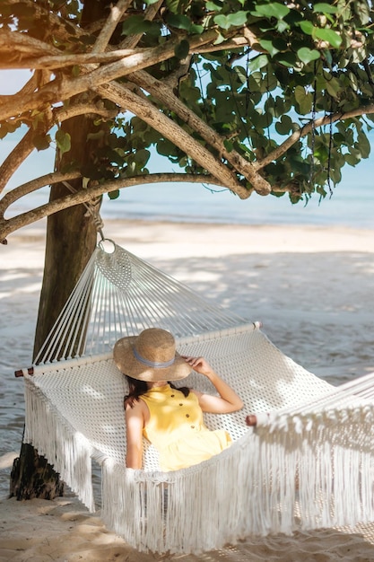 Happy Woman Traveller odpoczywa w hamaku na rajskiej plaży Turystka w żółtej sukience odpoczywa w pobliżu tropikalnego morza wakacje podróże lato Wanderlust i koncepcja wakacji