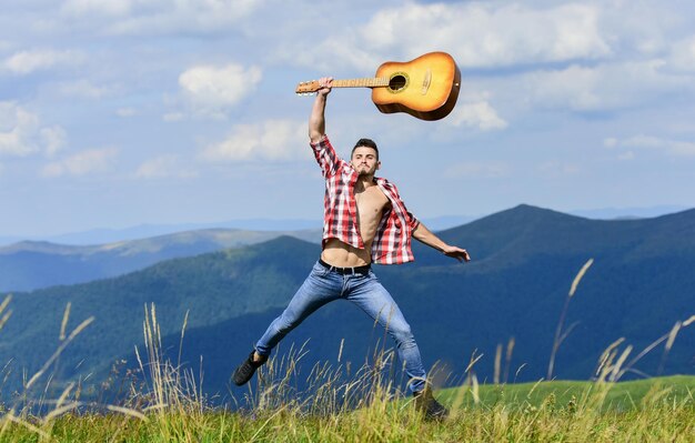 Hard rock western camping i piesze wędrówki szczęśliwy i wolny kowboj mężczyzna z nagim muskularnym tułowiem gitara akustyczna odtwarzacz muzyki country seksowny mężczyzna z gitarą w kraciastej koszuli moda hipster