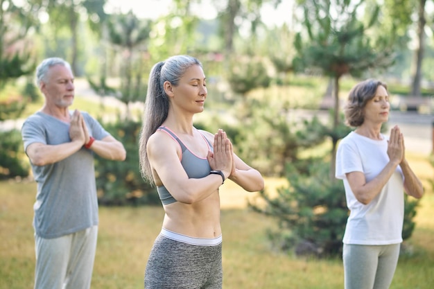 Harmonia. Ludzie w parku stoją z rękami w namaste i zamkniętymi oczami