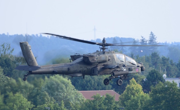 Helikopter leci przed drzewem, a z boku widnieje napis ah - 64.