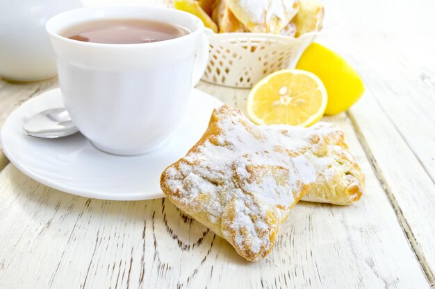 Herbata cytrynowa ciasteczka w białej filiżance na spodku cytryny na tle drewnianych desek
