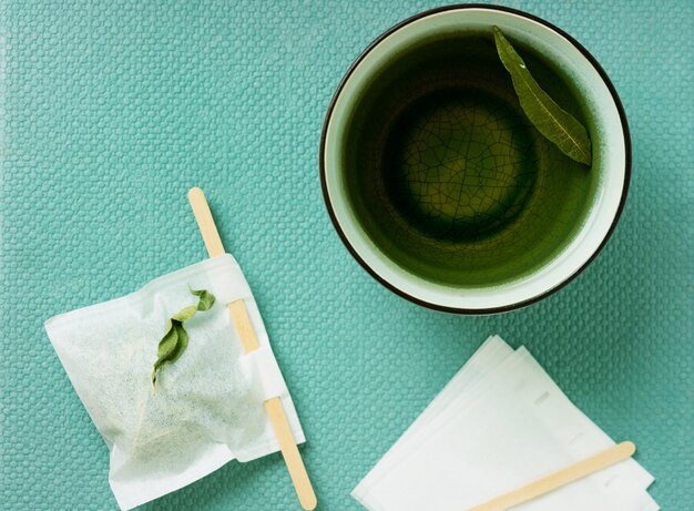 Zdjęcie herbata lemon verbena w kubku z ręcznie robioną torebką na zielonym biurku. widok z góry. flat lay