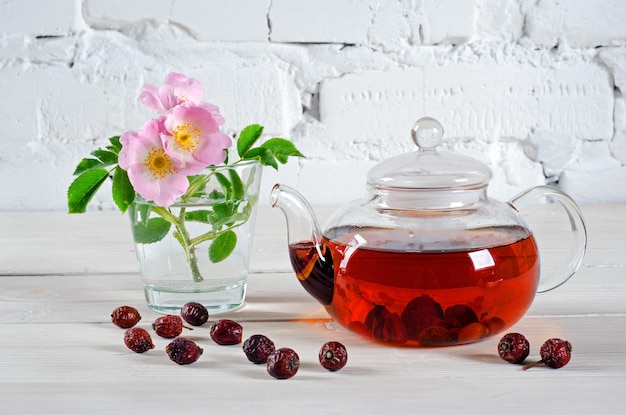 Herbata Teapot z owocami dzikiej róży i kwiatami dzikiej róży na białym drewnianym stole z miejscem na kopię tekstu