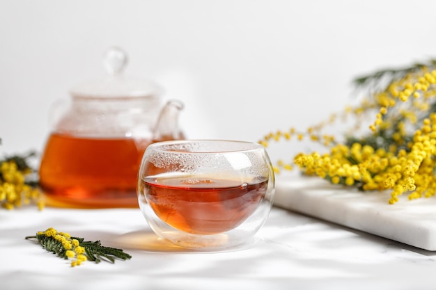 Herbata w Szklanej Filiżance i szklany czajniczek w Słoneczną Wiosnę z gałązką Mimozy