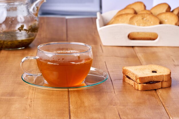 Herbata w szklanej filiżance na drewnianym stole i grzanka z powidłami śliwkowymi.