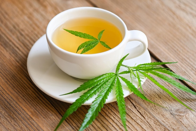 Herbata z konopi indyjskich ziołowa na filiżance z liśćmi marihuany liście marihuany zioła na drewnianym tle herbata zdrowotna z rośliną z liści konopi THC CBD zioła żywność i koncepcja medyczna