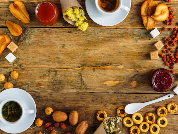Herbata ziołowa, suszone owoce i słodycze na starym drewnianym stole. W centrum miejsce na tekst.