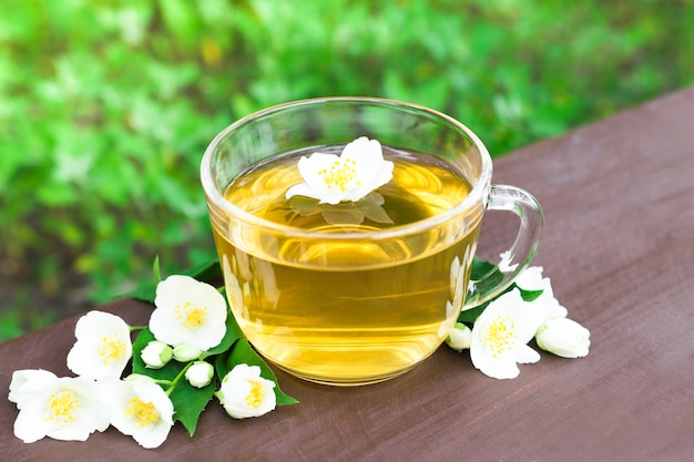 Zdjęcie herbata ziołowa w szklanym kubku z białymi kwiatami jaśminu zielonym naturalnym tłem