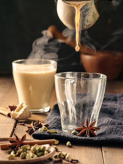Herbatę masala z przyprawami nalewa się do szklanych kubków na drewnianym stole.