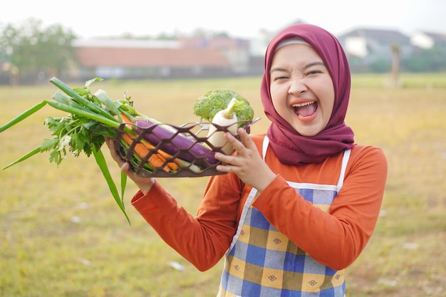 Hidżab kobieta wesoły nosić fartuch trzymać warzywa lewy gest
