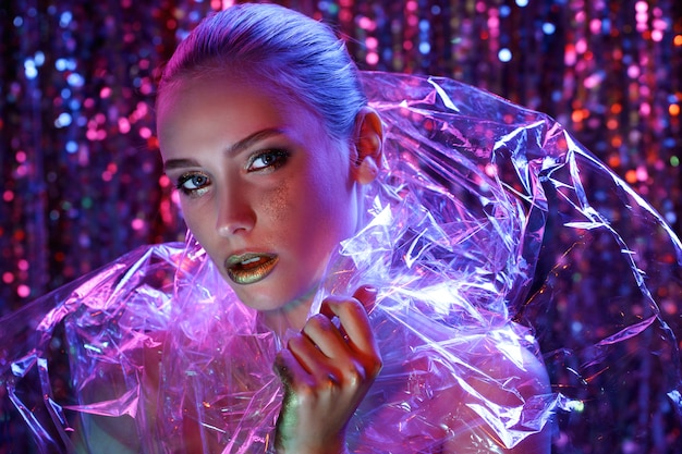 High Fashion model dziewczyna w kolorowe jasne neony pozowanie Studio przez przezroczysty film. Portret pięknej kobiety sexy w UV. Kolorowy makijaż artystyczny.