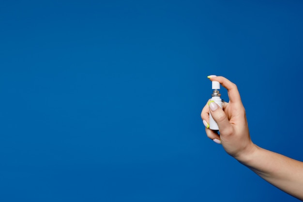 Higieniczny spray do dezynfekcji w schludnej kobiecej dłoni z manicure na niebieskim tle z miejsca kopiowania. Dezynfekcja rąk w schludnej kobiecej dłoni. Zdjęcie reklamujące higienę