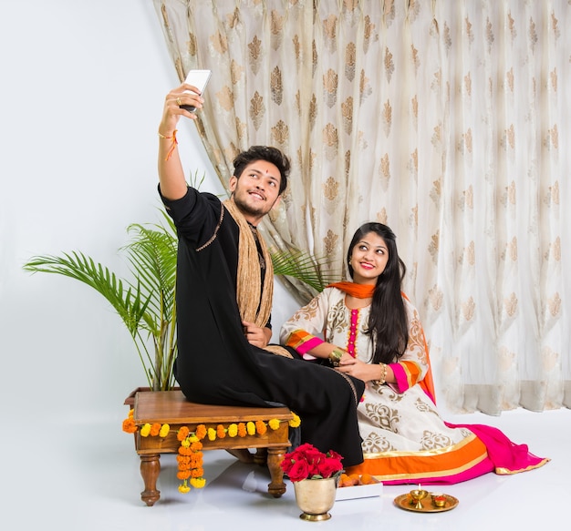 Hinduski młody brat i siostra świętujący festiwal Raksha Bandhan lub Rakhi lub na Bhai dooj lub Bhau-Beej z Poja Thali, słodyczami, prezentami lub robieniem zdjęć selfie