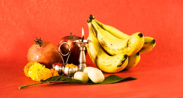 Hinduskie elementy puja, diya, haldi kumkum, jabłko, granat i banan jako ofiara bogu i indyjskiej słodkiej pedhy w widoku z góry srebrnej miski, odizolowane na czerwonej powierzchni