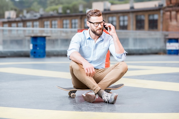 Hipster biznesmen rozmawia z inteligentnym telefonem na placu zabaw na dachu budynku przemysłowego. Koncepcja biznesowa stylu życia