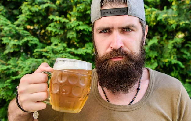Zdjęcie hipster brutalny brodaty mężczyzna trzyma kubek zimnego świeżego piwa mężczyzna delektujący się piwem latem alkohol i koncepcja baru kreatywny młody piwowar piwo rzemieślnicze to młode miejskie i modne odrębna kultura piwa
