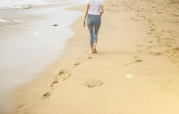 Hipster dziewczyna idzie na plażyPiękny widok na morze Duże fale nad oceanem Linia brzegowa ze śladami stóp Wakacje letnie Koncepcja podróży