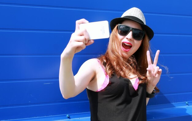 Hipster dziewczyna przy niebieskiej ścianie robi selfy