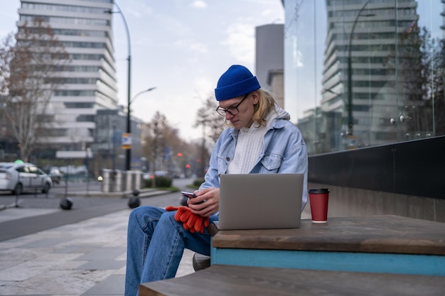 Hipster facet freelancer ze smartfonem i laptopem na zewnątrz