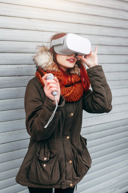 Hipster młoda dziewczyna gra w mobilną grę wirtualnej rzeczywistości na smartfonie podłączonym do nowoczesnych okularów VR na zewnątrz
