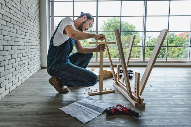 Hipster młody człowiek pracujący jako złota rączka patrząc na instrukcję podczas montażu drewnianego stołu z wyposażeniem, koncepcja domu diy i samoobsługi. w biurze.