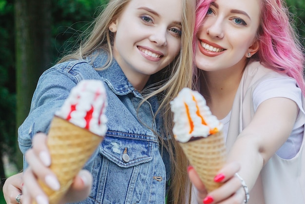 Zdjęcie hipster młodzi dorośli przyjaciele obejmując się podczas spędzania czasu w mieście. dwie młode kobiety, śmiejąc się i spacerując, ciesząc się beztroskim, wakacyjnym stylem życia. dwie ładne dziewczyny jedzą lody na mieście