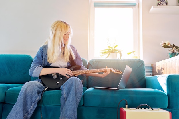 Hipster nastolatek dziewczyna gra na gitarze elektrycznej, patrząc na monitor laptopa