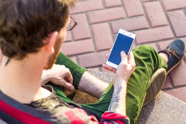 Hipster z tatuażem używa telefonu na ulicy