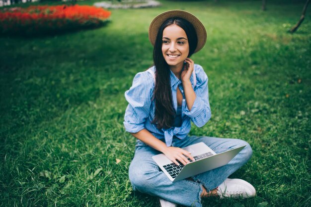 hipsterska dziewczyna odpoczywa na zielonej trawie, ciesząc się wolnym czasem na komunikację online