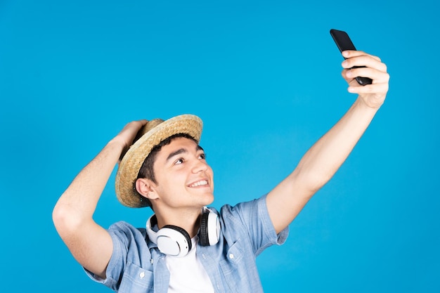 Hiszpanie nastolatek turysta chłopiec robi selfie za pomocą telefonu na białym tle na niebieskim tle