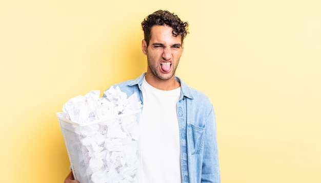 Hiszpanie przystojny mężczyzna czuje się zniesmaczony i zirytowany, a koncepcja kosza na śmieci z papierowymi kulkami wysuwa język