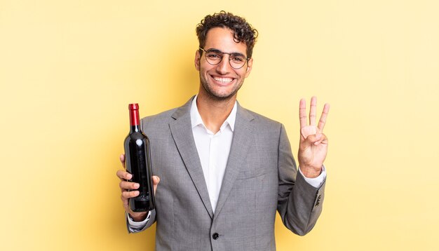 Hiszpanie przystojny mężczyzna uśmiecha się i wygląda przyjaźnie, pokazując numer trzy. koncepcja butelki wina