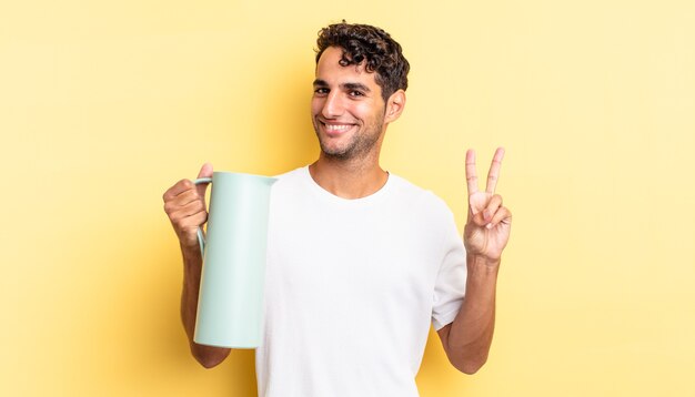Hiszpanie przystojny mężczyzna uśmiechający się i wyglądający przyjaźnie, pokazując numer dwa. koncepcja termosu do kawy