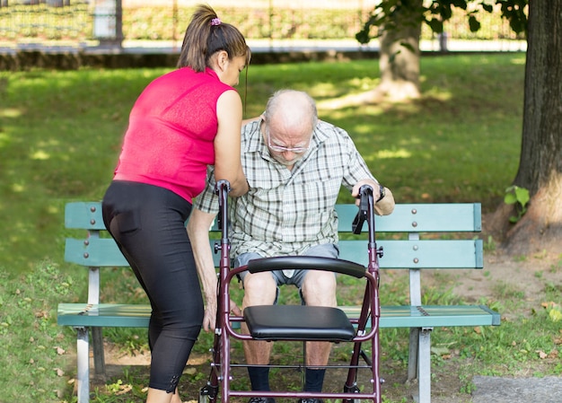 Hiszpański opiekun pomaga starszemu mężczyźnie usiąść na ławce w parku