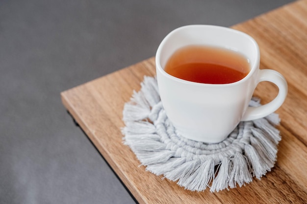 Hobby handmade makrama Herbata w filiżance na szarym stojaku makramy na drewnianym stole