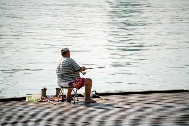 Hobby wędkarskie, rybak siedzący na skarpie miejskiej rzeki i łowiący ryby