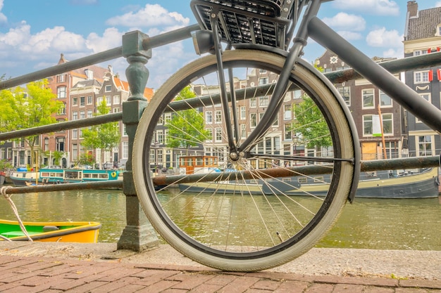 Zdjęcie holandia letni dzień w amsterdamie widok przez koło rowerowe na nabrzeże kanału z autentycznymi domami lądowymi i łodziami mieszkalnymi w pobliżu brzegu.