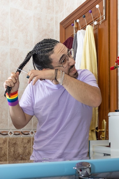 Homoseksualista z warkoczami obcinającymi włosy przed lustrem wesoły obcinający włosy nożyczkami Osoba obcinająca własne włosy przed lustrem