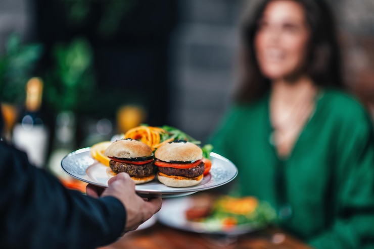 Zdjęcie horyzontalny obraz męskiego kelnera serwującego talerz wegetariańskiego hamburgera pięknej uśmiechniętej młodej kobiecie w restauracji