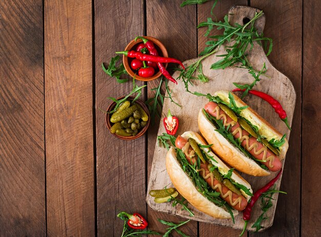 Hot dog z pickles, kaparami i arugula na drewnianym tle.