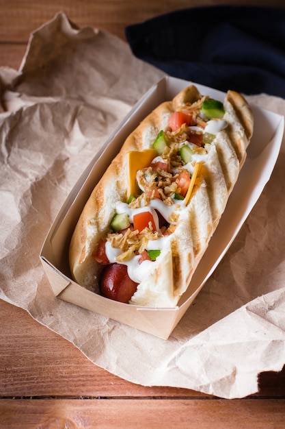 Hot dog z serem, kiełbasą, smażoną cebulą, warzywami i sosem