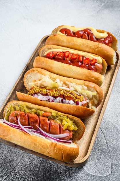 Hot dogi pełne z dodatkami na tacy. Pyszne hot-dogi z kiełbasą wieprzową i wołową. Białe tło. Widok z góry